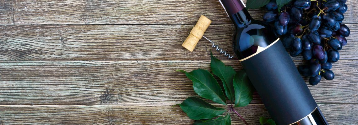 Bottle with red wine, corkscrew, blue grapes, leaves on a wooden table. Wine background with copy space. Top view, flat lay