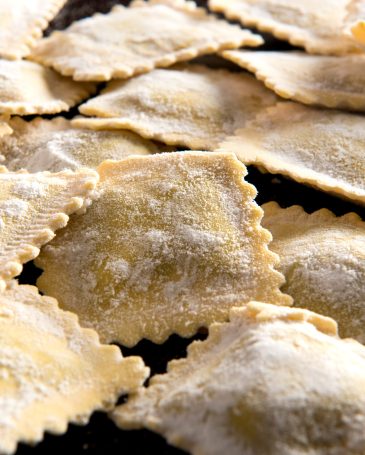 Close-up of rectangular shape raw handmade Italian ravioli pasta with dough on black surface